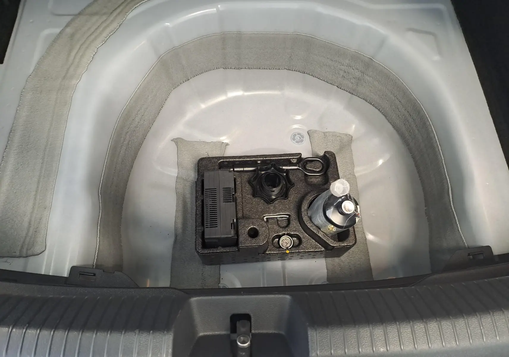 Coffre ouvert d'un Volkswagen Taigo blanc pur, vue plongeante sur le rangement d'outils et compresseur intégré.