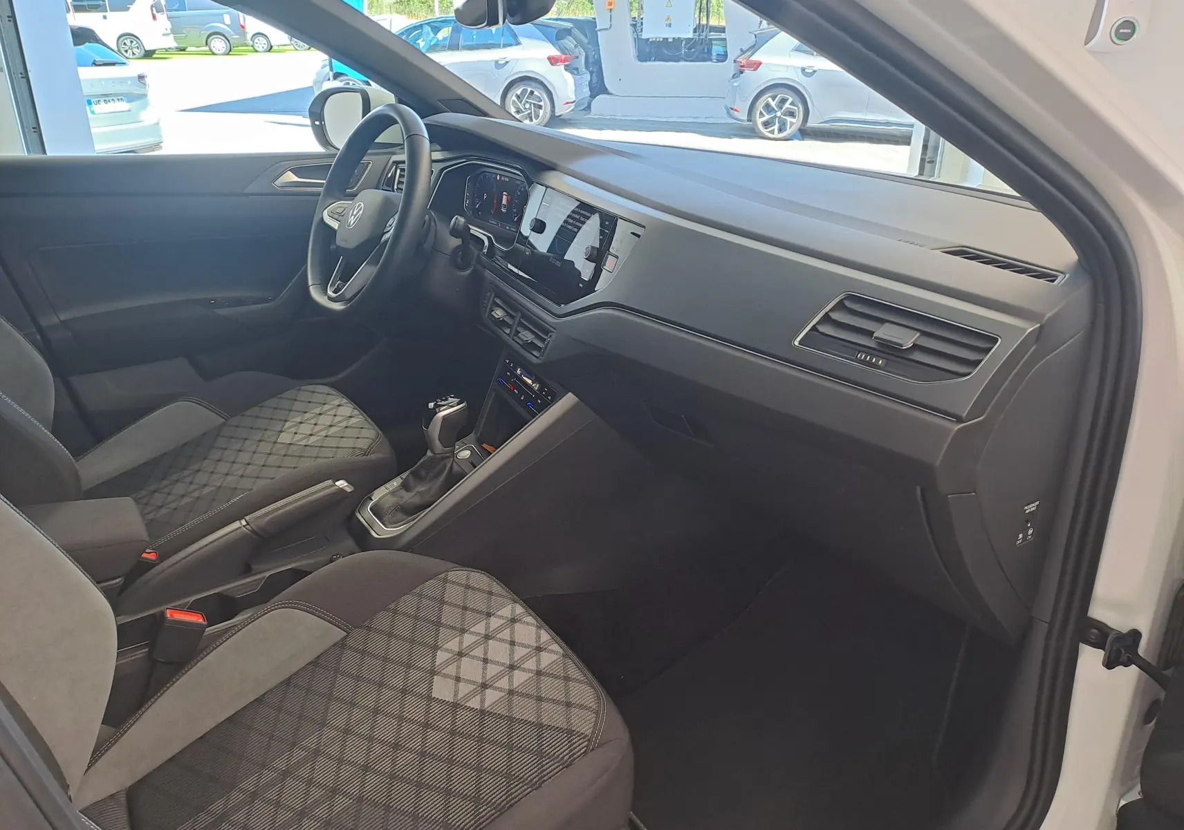 Vue intérieure côté conducteur du Volkswagen Taigo 2025, montrant le tableau de bord noir et les sièges tissu à motif géométrique.