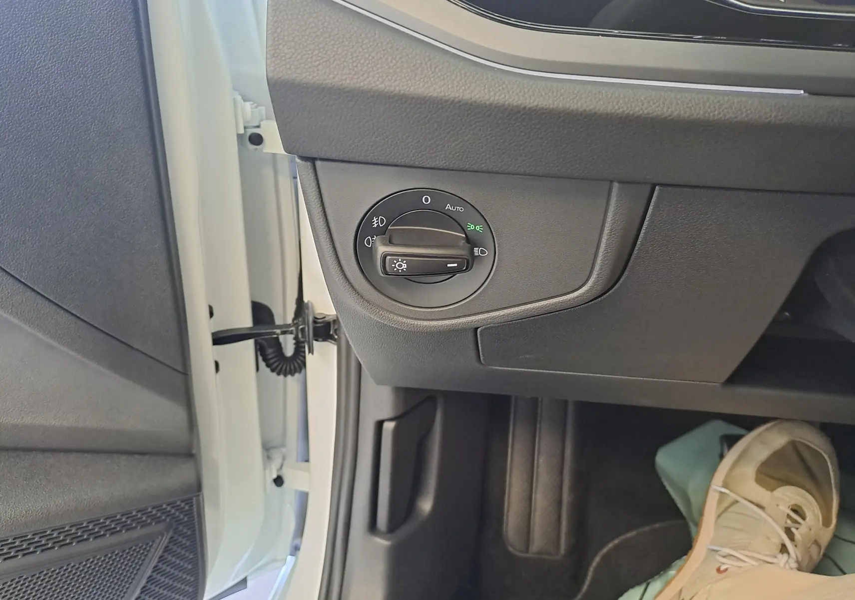 Vue intérieure côté gauche du tableau de bord du Volkswagen Taigo blanc, avec commande d'éclairage et partie de la portière ouverte.