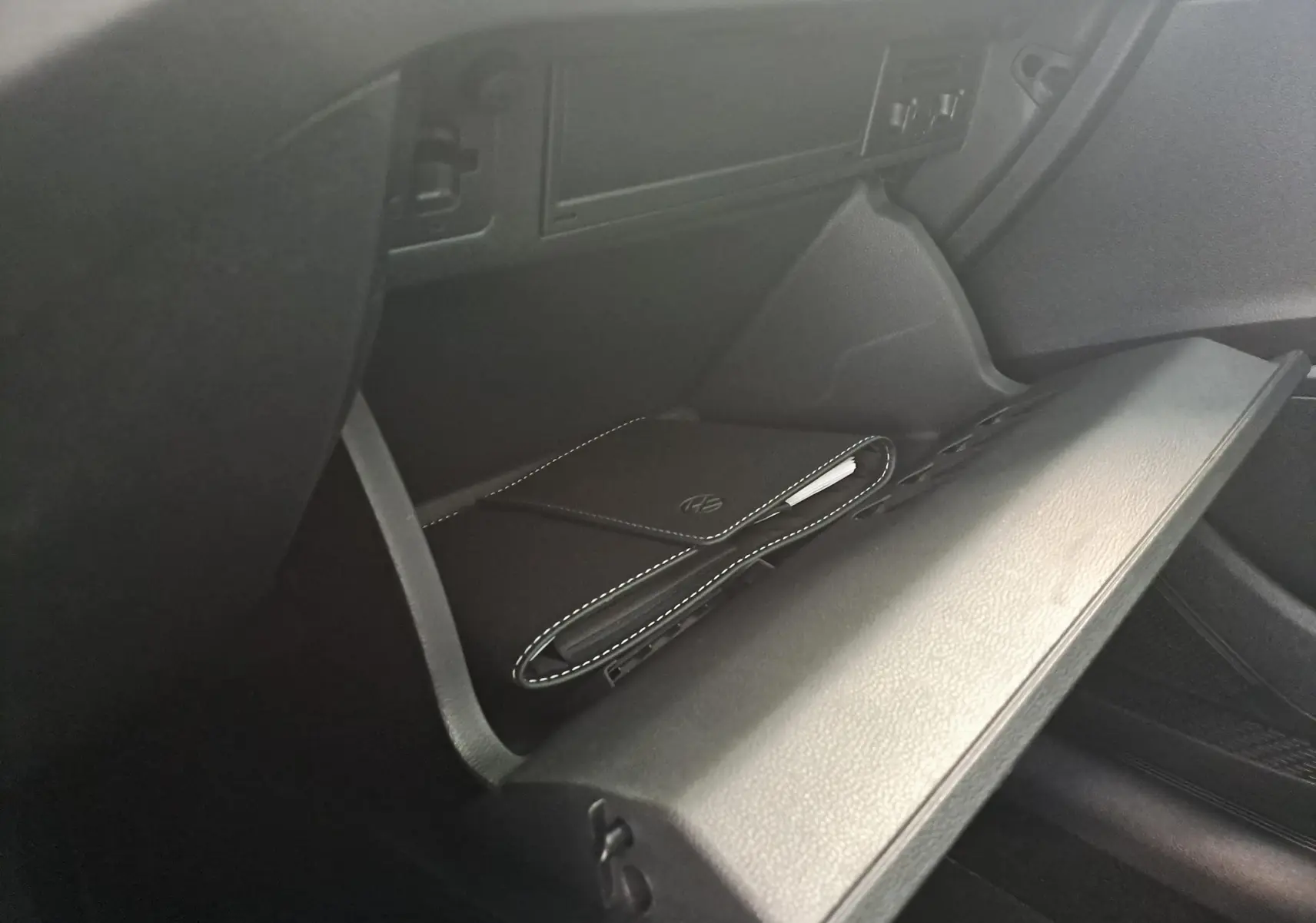 Gant de boîte à gants ouvert côté passager du Volkswagen Taigo avec pochette noire au logo VW visible.