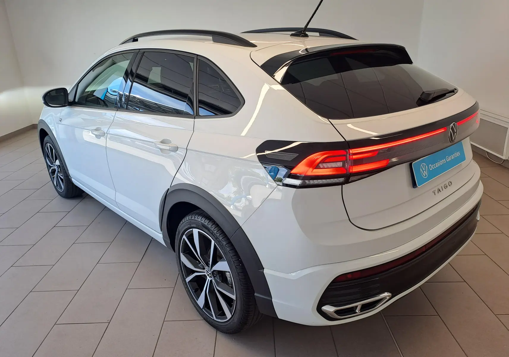 Vue 3/4 arrière droite du Volkswagen Taigo blanc pur avec jantes alliage 18 pouces et feux arrière LED allumés.