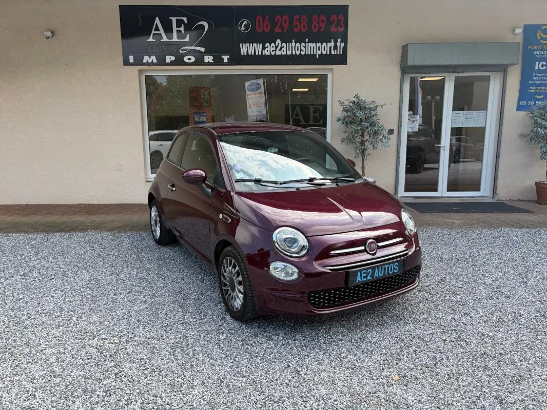 Fiat 500 violet vue 3/4 avant droit, berline compacte avec jantes alliage et calandre chromée devant un garage.