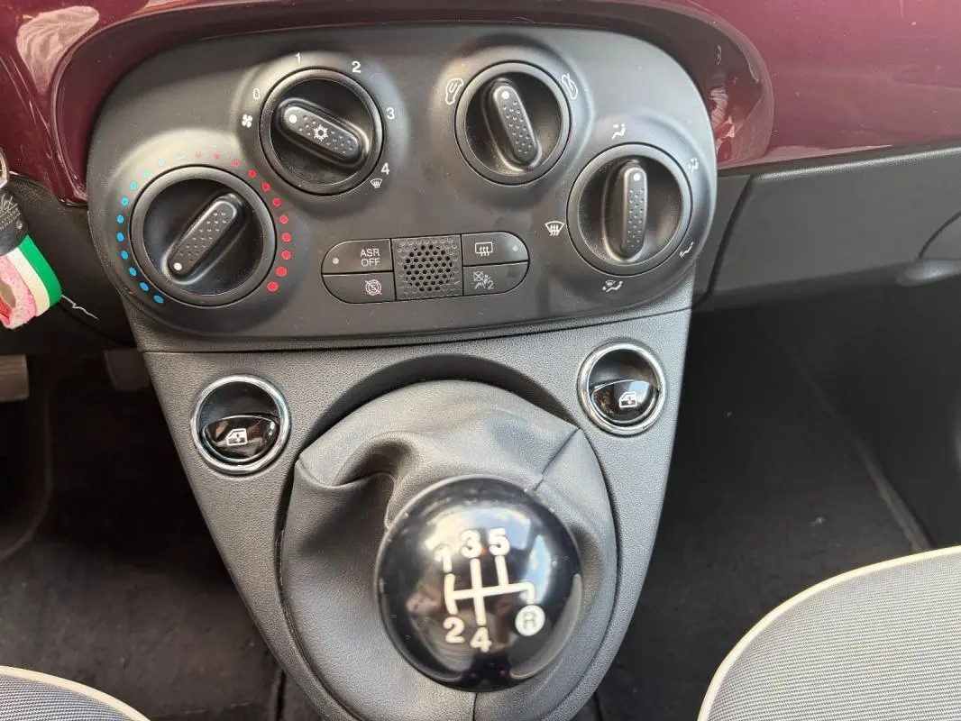 Vue rapprochée de la console centrale violette d'une Fiat 500 2019 avec commandes de climatisation et levier de vitesse manuel.