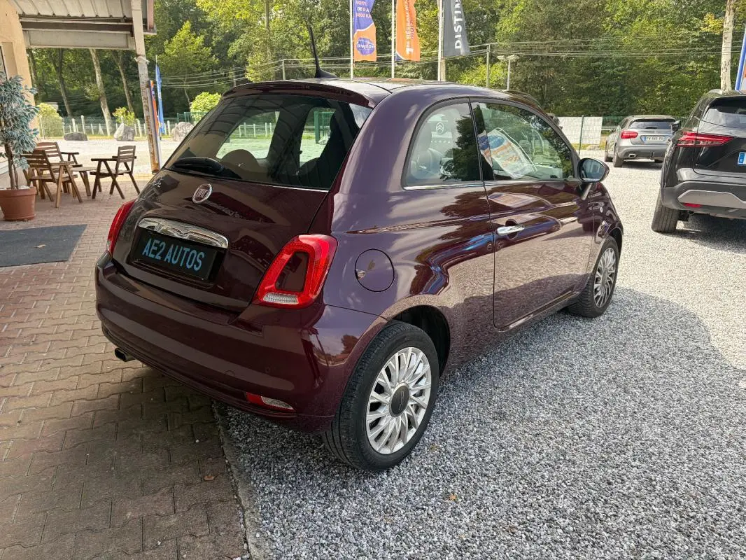 Vue 3/4 arrière droite d'une FIAT 500 berline violet foncé avec jantes alliage, stationnée sur un sol gravillonné.