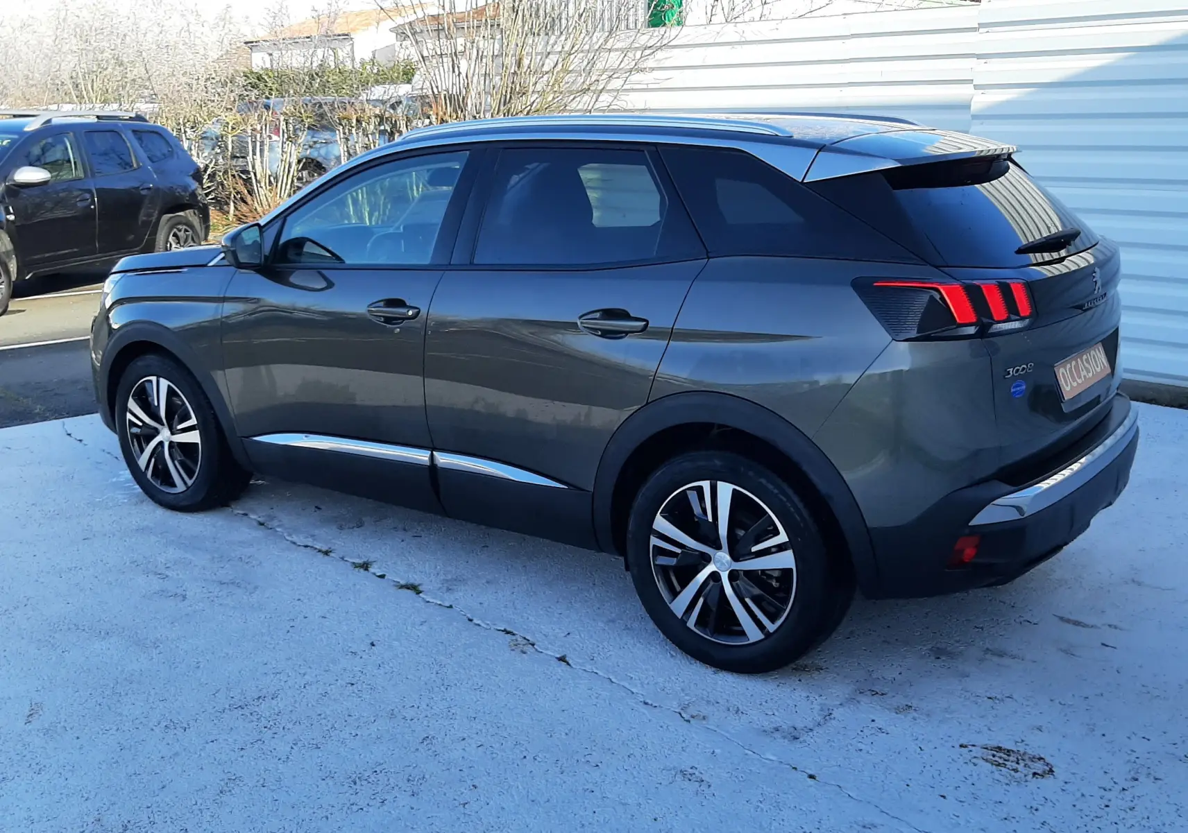 Peugeot 3008 gris Amazonite en vue 3/4 arrière droit, avec jantes alliage et feux arrière à griffes rouges.