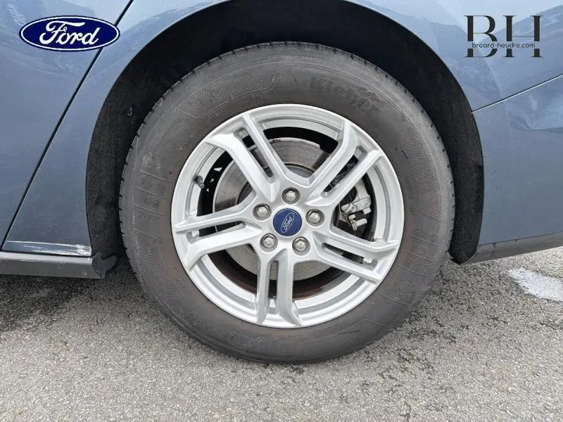 Gros plan sur la roue avant gauche avec jante alu argentée d'une Ford Focus SW Bleu Azur métallisé.