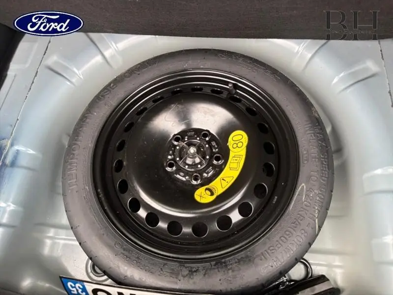 Vue en plongée sur la roue de secours noire dans le coffre d'une Ford Focus SW bleu azur métallisé de 2019.