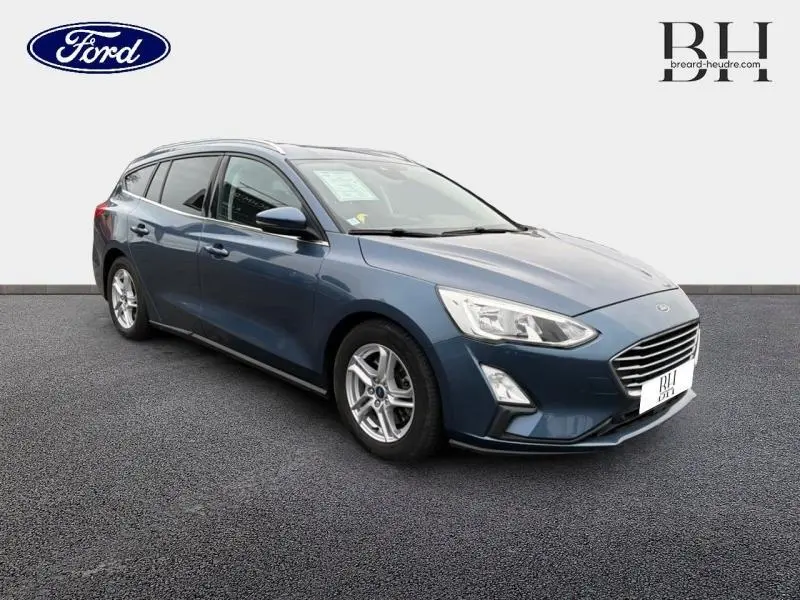 Ford Focus SW bleu azur métallisé vue 3/4 avant droit avec jantes alu et barres de toit visibles.