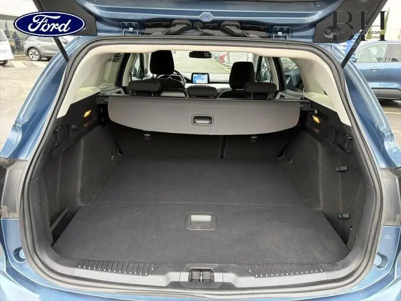 Coffre ouvert vu de l'arrière d'une Ford Focus SW 1.5 EcoBlue bleu azur métallisé avec cache-bagages et intérieur noir.
