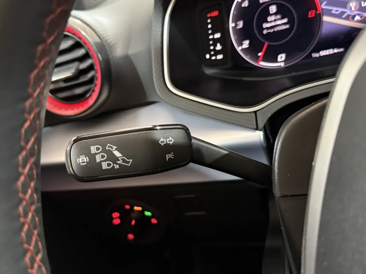 Gros plan sur la manette de clignotants à gauche du volant cuir rouge de la SEAT Ibiza 2024, tableau de bord numérique visible.