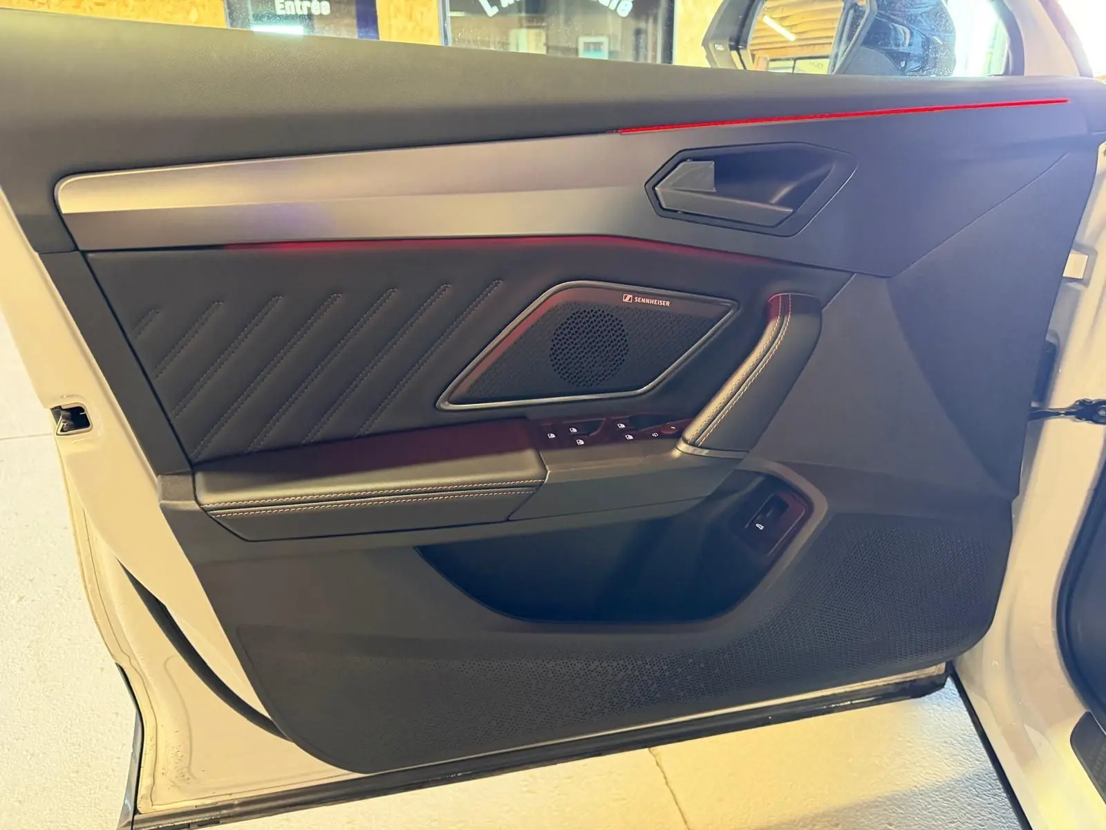 Vue intérieure côté porte avant gauche d'une CUPRA Formentor blanche, avec haut-parleur Sennheiser et éclairage d'ambiance rouge.