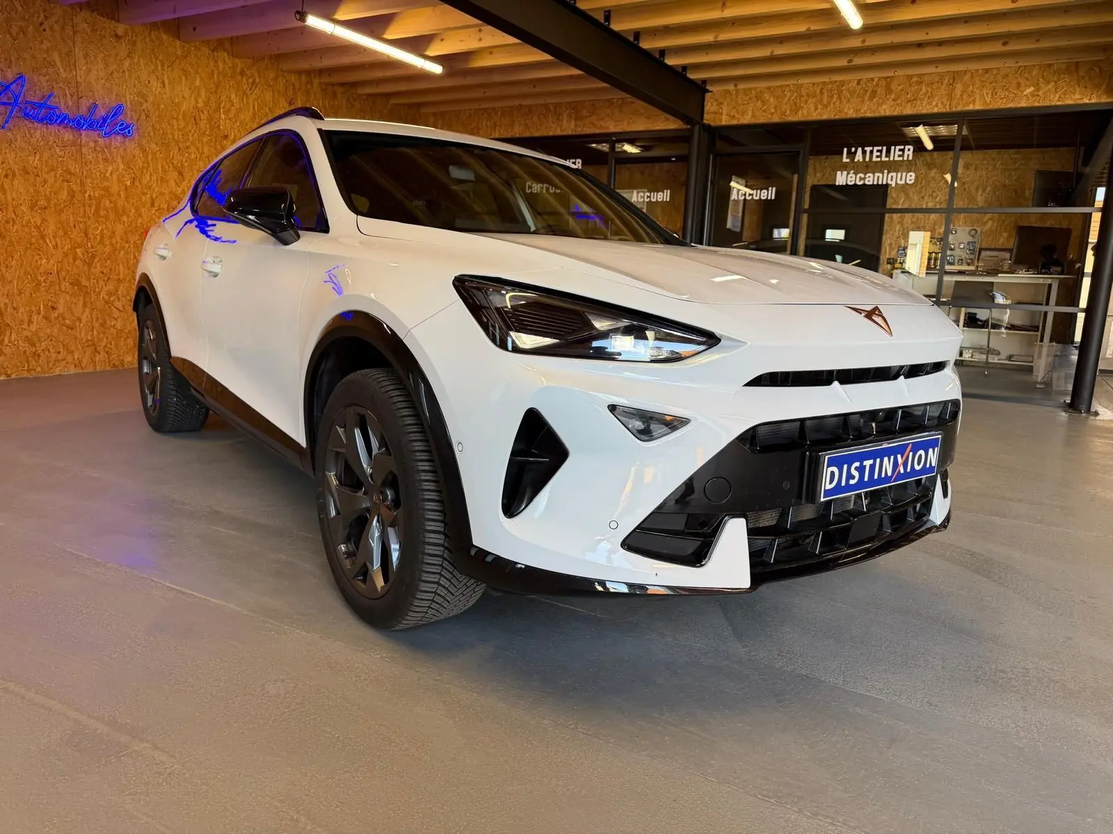 Vue 3/4 avant d'une CUPRA Formentor blanche avec détails noirs, calandre marquée et jantes foncées en showroom.