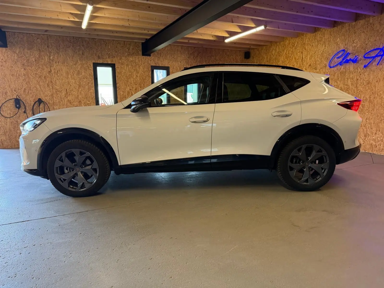 Vue de profil côté gauche d'un CUPRA Formentor blanc 2025 avec jantes noires et vitres arrière surteintées dans un garage.