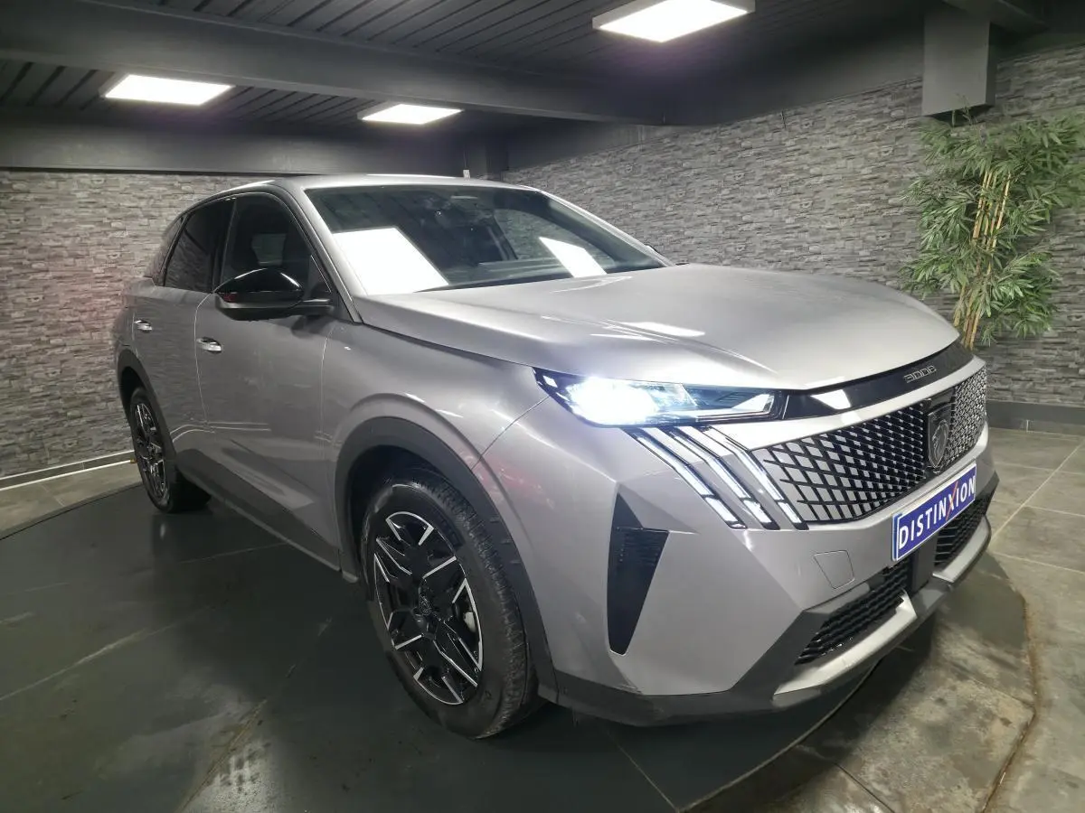 Peugeot 3008 gris métallisé en 3/4 avant droit, avec calandre noire et phares LED allumés dans un showroom.