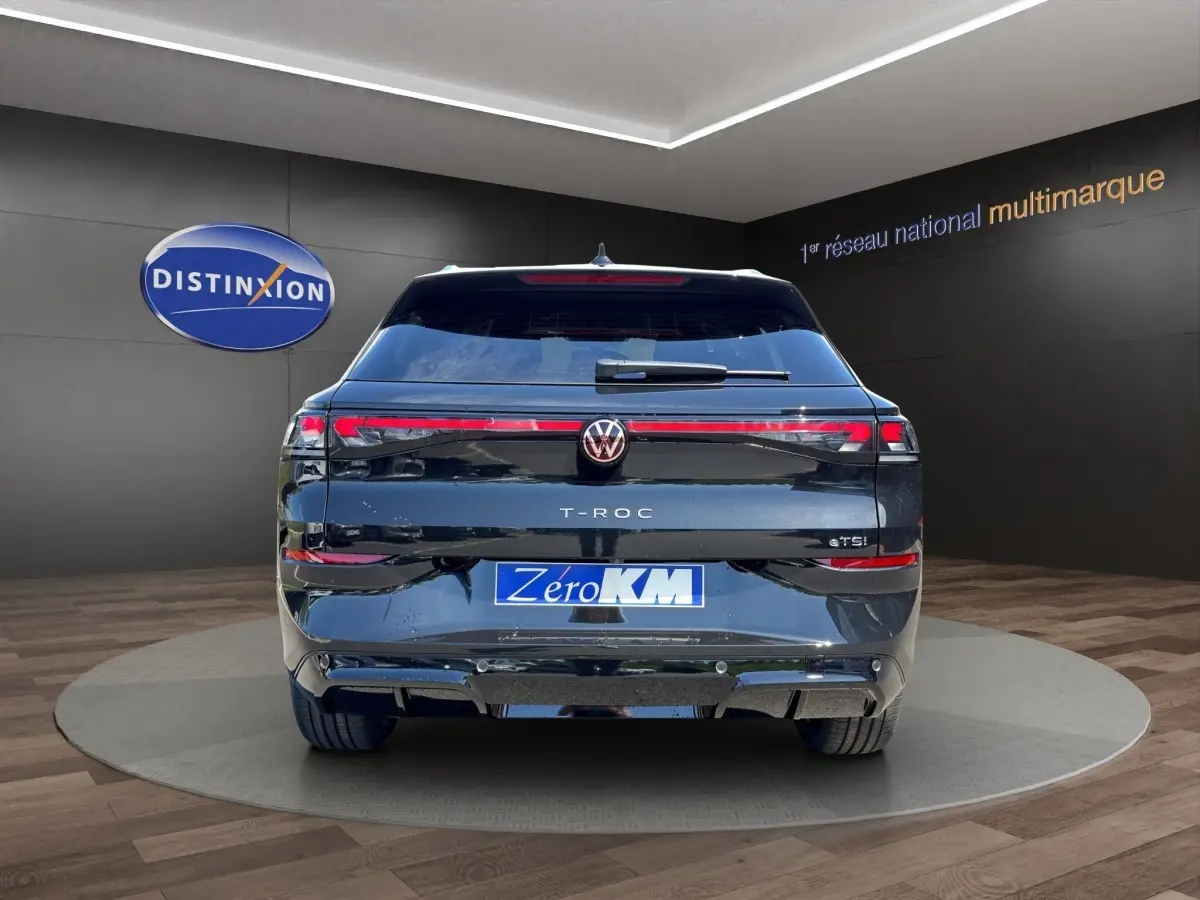Vue arrière d'un Volkswagen T-Roc noir 2026 avec feux LED et attelage visible dans un showroom.