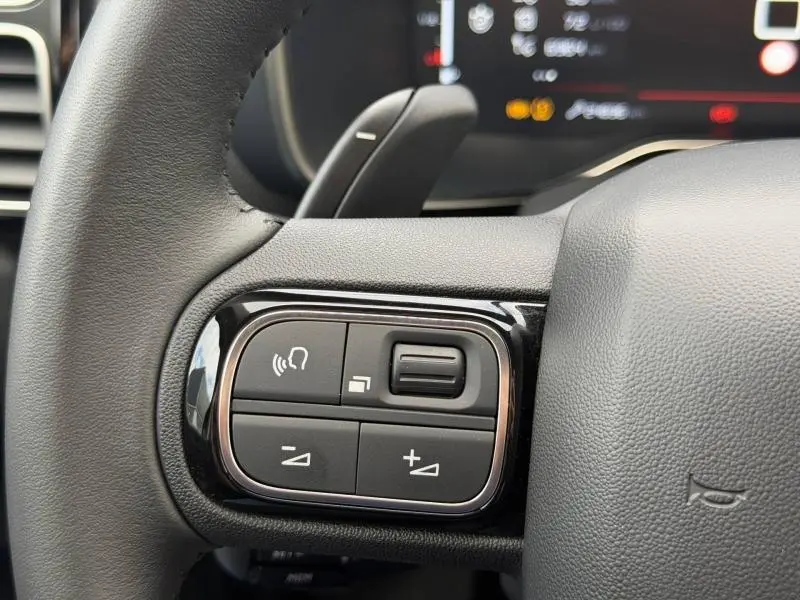 Gros plan sur les commandes noires du volant cuir du Citroën C5 Aircross 2024 Hybride, avec finition brillante.