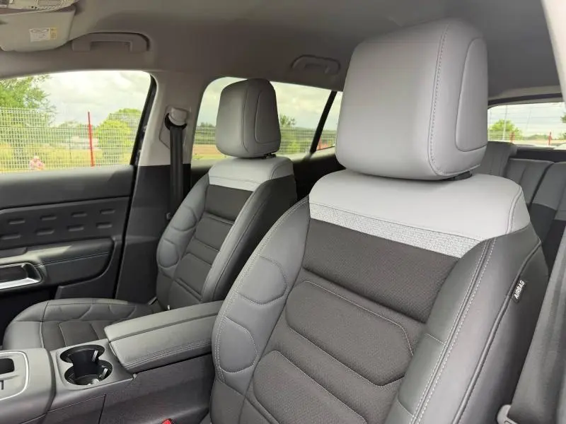 Vue intérieure rapprochée des sièges avant gris clair et noir du Citroën C5 Aircross 2024 avec accoudoir central et porte-gobelets.