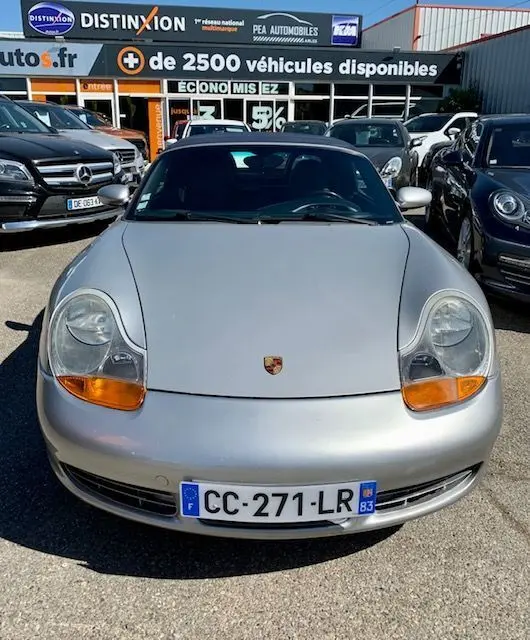 Vue frontale d'une Porsche Boxster 986 gris clair de 2001, avec phares ovales et plaque d'immatriculation française visible.