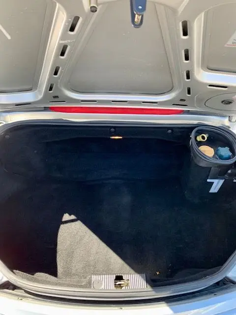 Coffre ouvert vu de dessus du Porsche Boxster 986 gris 2001, montrant l'intérieur noir et un compartiment latéral.