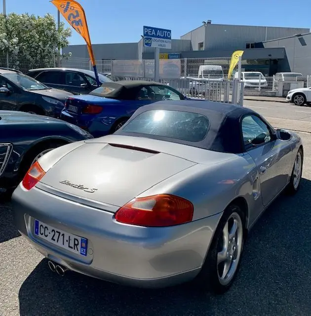 Vue 3/4 arrière droite d'une Porsche Boxster 986 gris métallisé de 2001 avec capote noire et double sortie d'échappement.