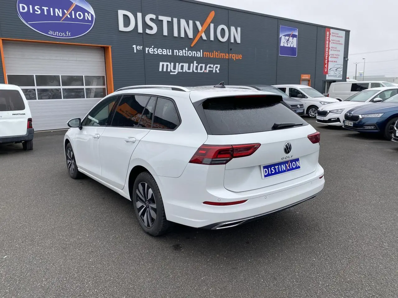 Volkswagen Golf SW blanc oryx vue 3/4 arrière droit avec vitres arrière surteintées sur parking de concession.