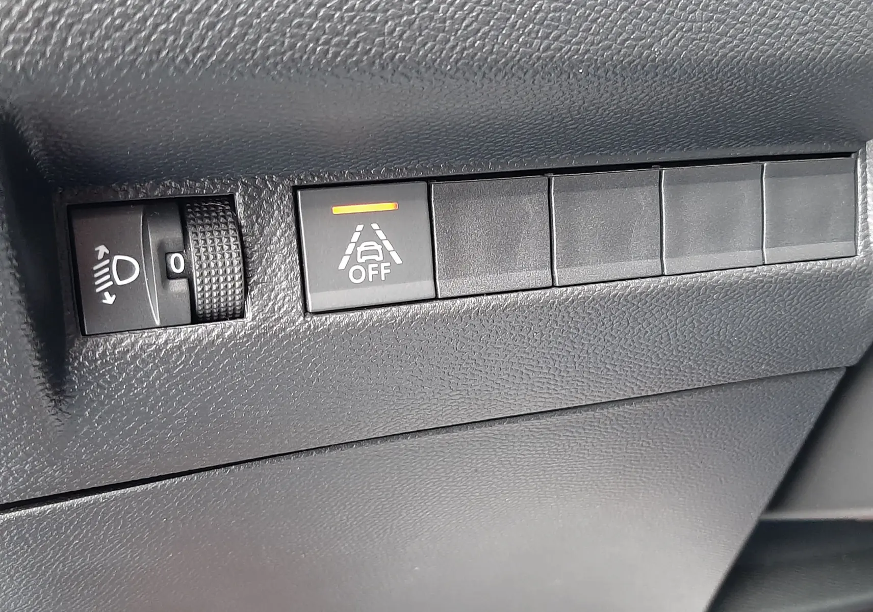Gros plan sur les commandes de réglage des phares et d'alerte de maintien de voie dans l'habitacle noir du Peugeot 2008 gris.