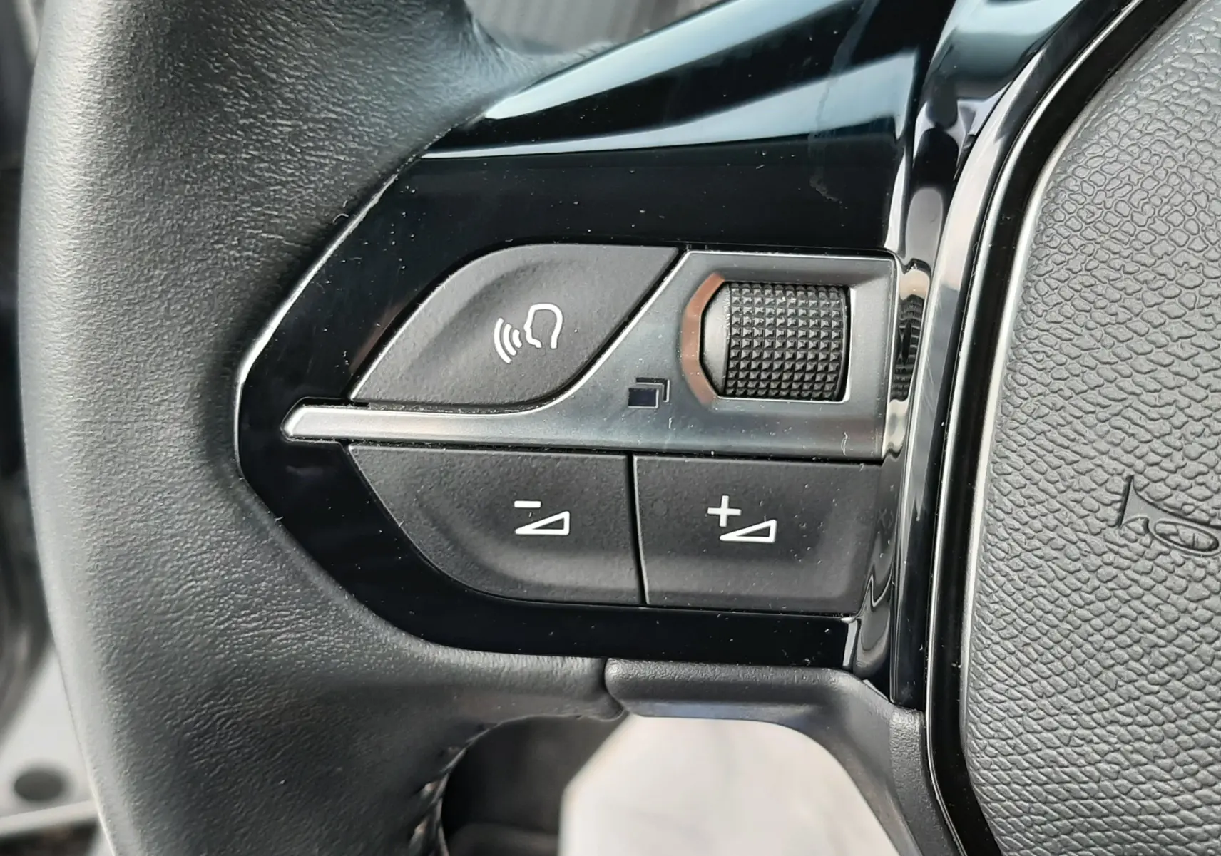 Gros plan sur les commandes de volume et téléphone sur le volant noir du Peugeot 2008 gris 2021.