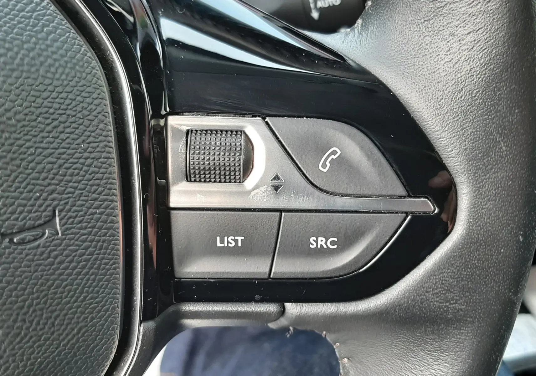 Gros plan sur les commandes gauche du volant noir du Peugeot 2008 gris 2021, avec boutons LIST, SRC et téléphone.
