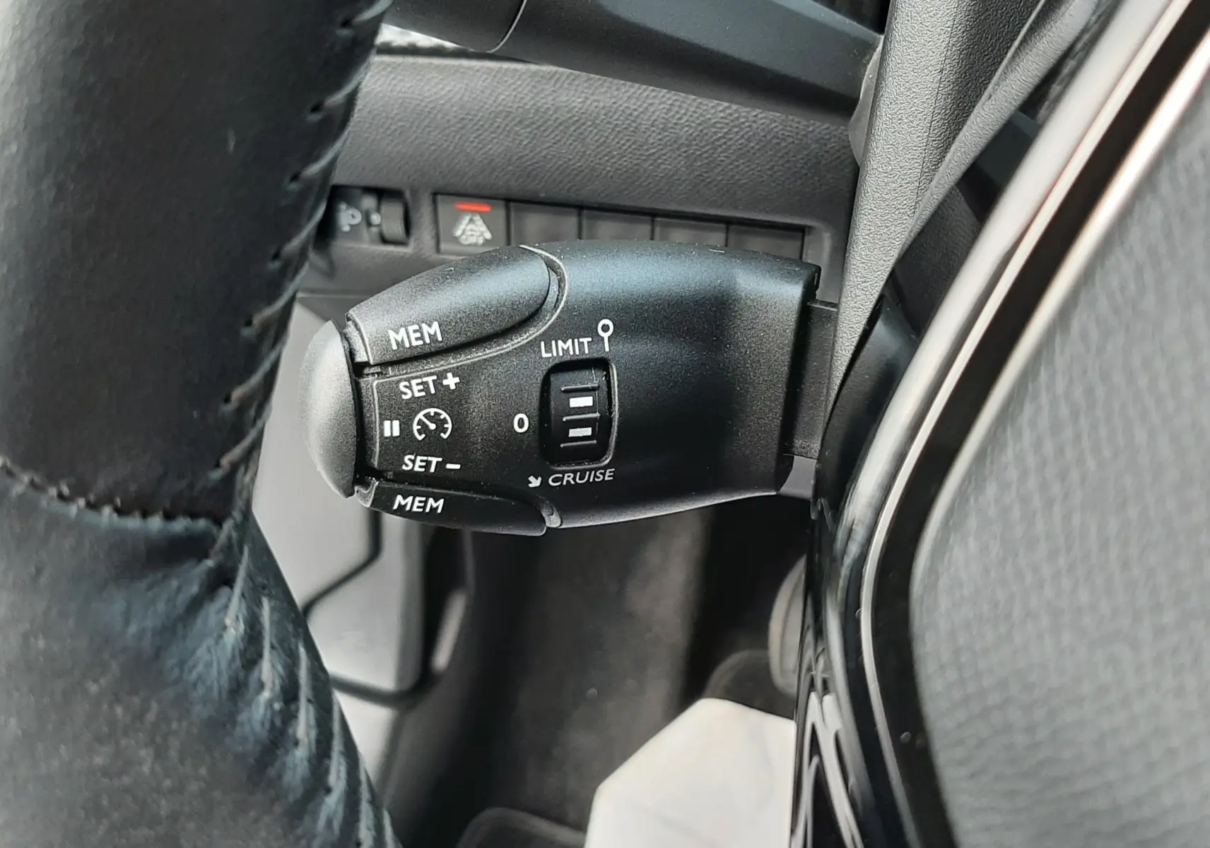 Gros plan sur la commande de régulateur de vitesse noire à gauche du volant d'un Peugeot 2008 gris 2021.