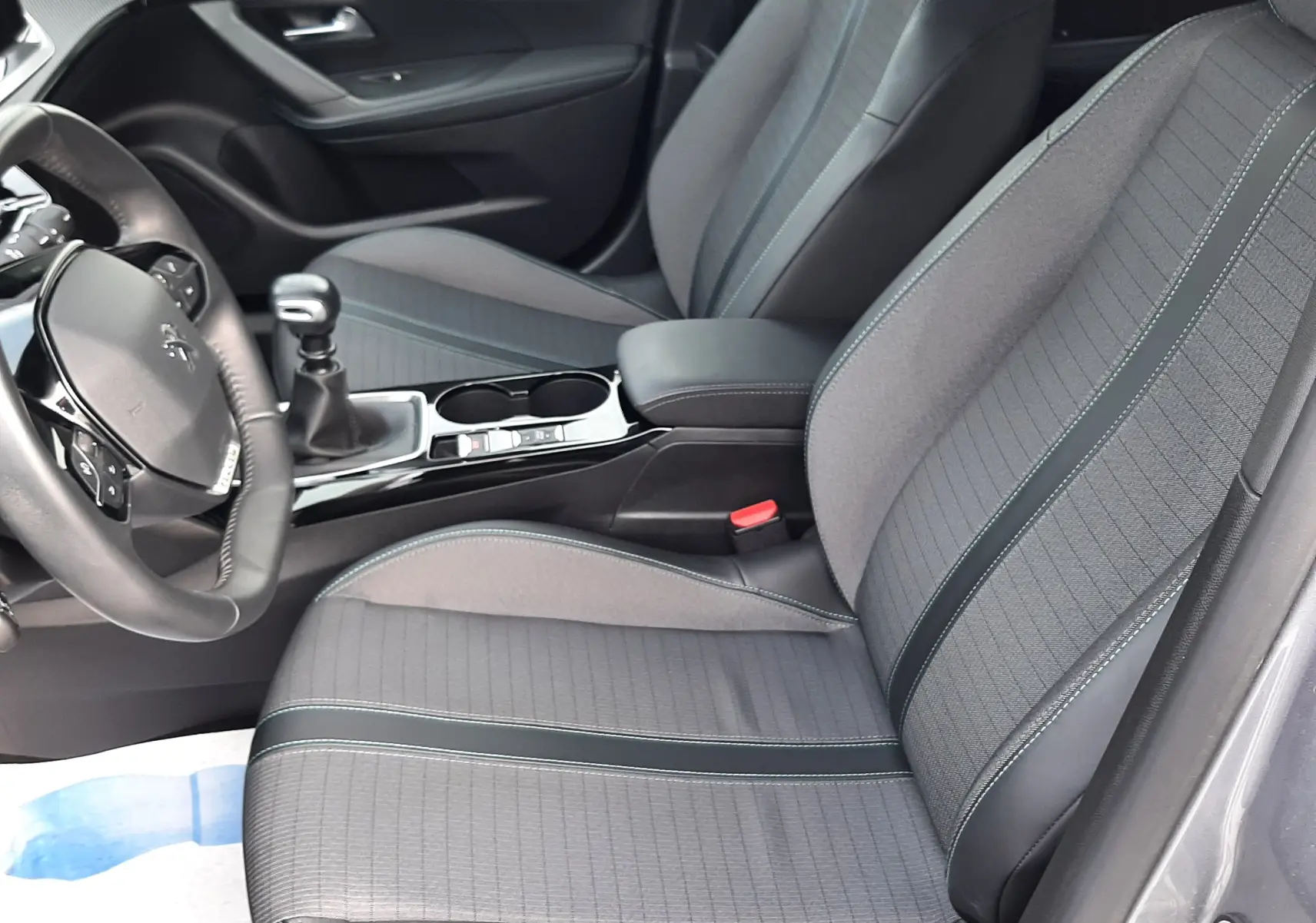 Vue intérieure côté conducteur du Peugeot 2008 gris 2021, sièges tissu gris avec surpiqûres et levier de vitesse manuel.