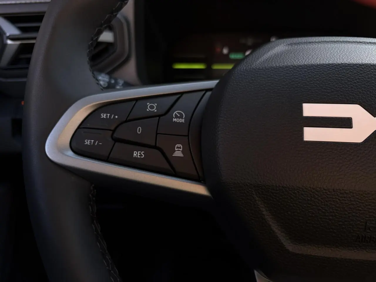 Gros plan sur les commandes gauche du volant noir du Dacia Duster 2026, avec logo Dacia visible au centre.