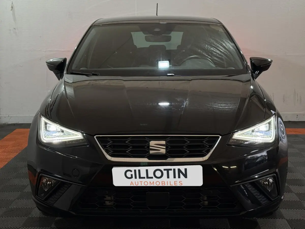 Vue avant d'une SEAT Ibiza 1.0 TSI 110 FR noire avec phares LED allumés dans un showroom.