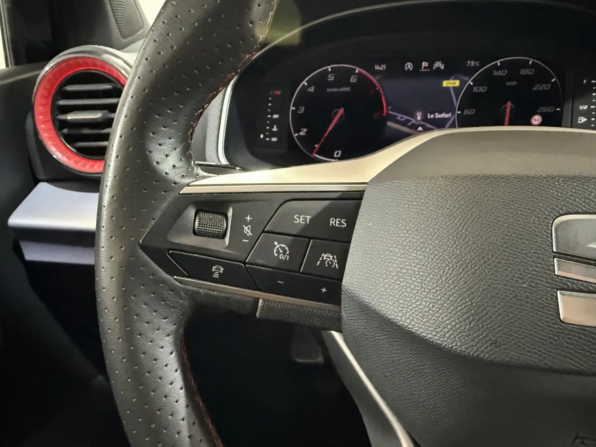 Gros plan sur le volant cuir et alu noir de la SEAT Ibiza 2024, avec commandes multifonctions et tableau de bord numérique.