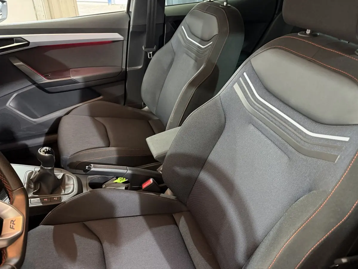 Vue intérieure côté conducteur de la SEAT IBIZA 1.0 TSI 110 FR 2024 noire, sièges sport avec surpiqûres orange et volant multifonction cuir alu.