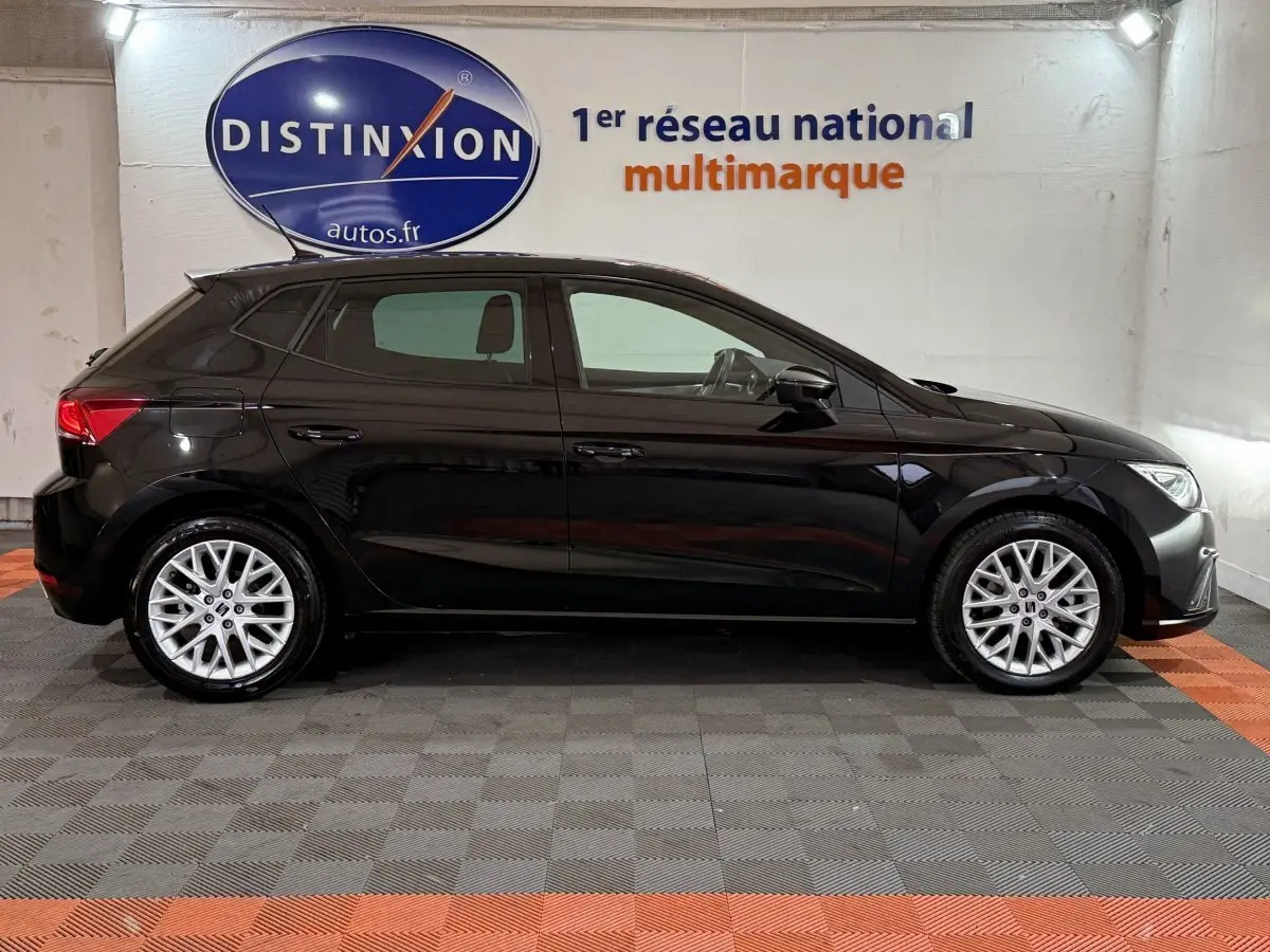 Profil droit d'une SEAT Ibiza 1.0 TSI 110 FR noire, avec jantes alliage argent et vitres teintées, en intérieur showroom.