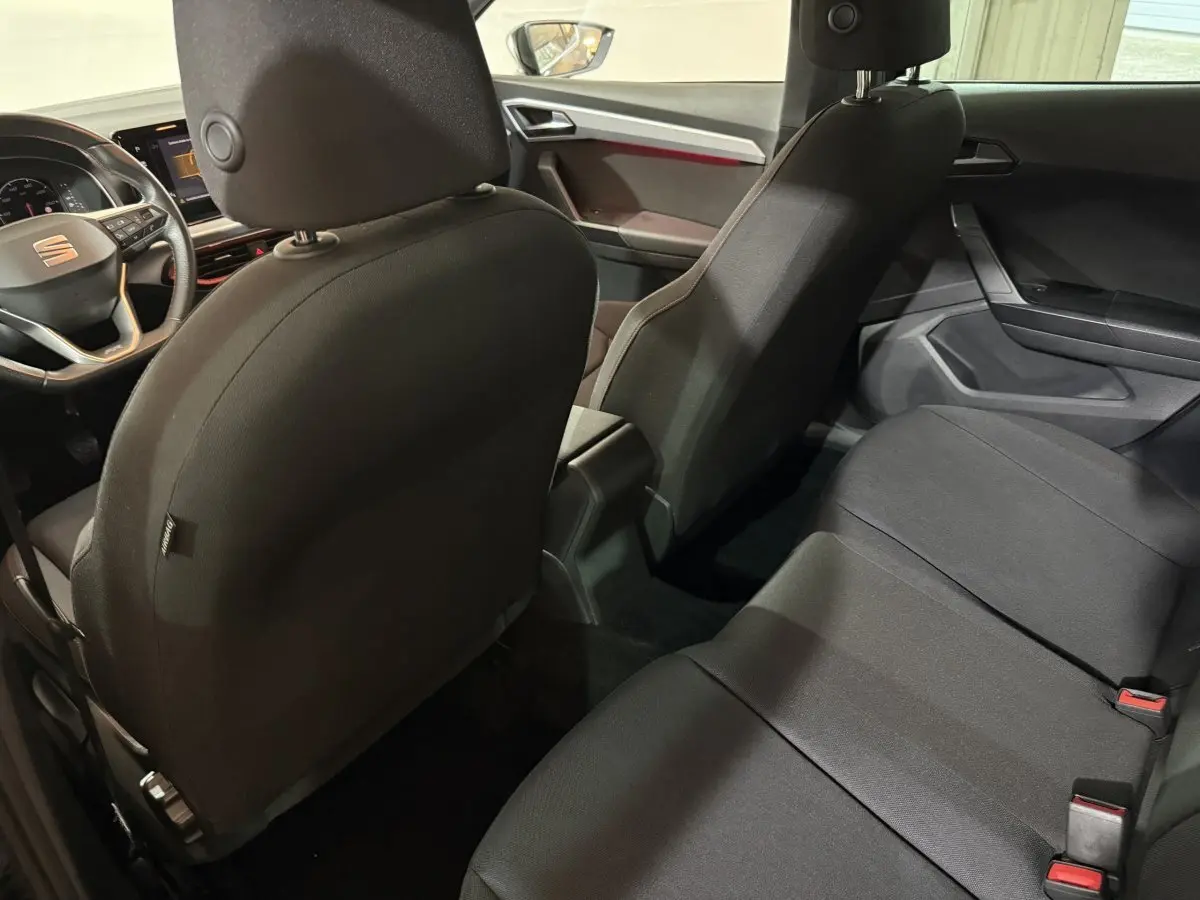 Vue intérieure arrière de la SEAT IBIZA 1.0 TSI 110 FR 2024 noire, montrant les sièges tissu noirs et le tableau de bord partiel.