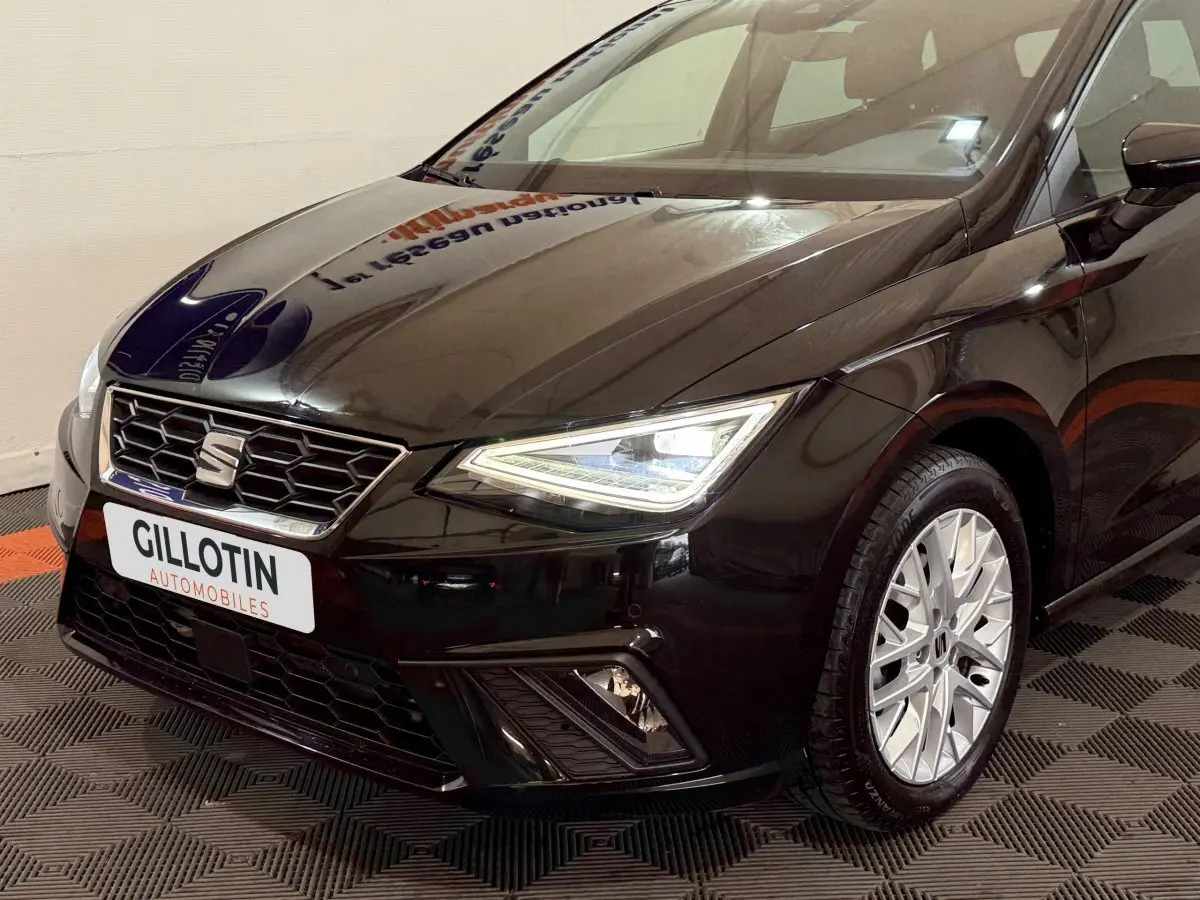 Vue 3/4 avant droit d'une SEAT Ibiza noire 2024 avec phares LED allumés et jantes argentées détaillées.