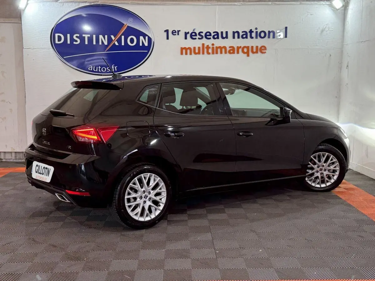 Vue 3/4 arrière droite d'une SEAT Ibiza noire 2024 avec jantes alliage et feux arrière LED allumés.