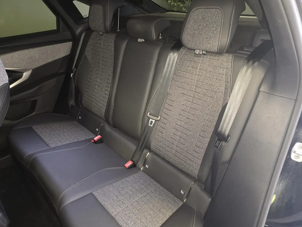Vue intérieure côté gauche des sièges arrière gris tissu et noir cuir du Peugeot 3008 hybride 2025 avec ceintures de sécurité visibles.