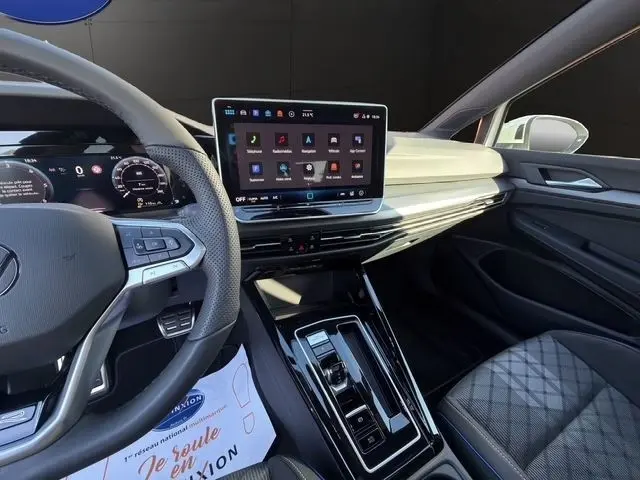Vue intérieure côté conducteur de la Volkswagen Golf 2.0 TDI 150 DSG7 R-Line blanche, avec écran tactile central et volant multifonctions.