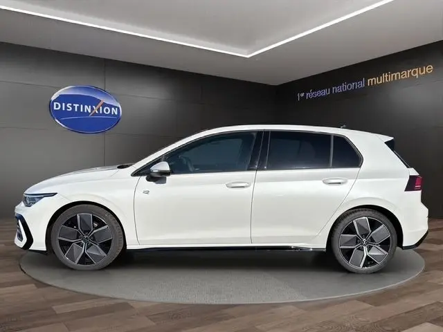 Vue de profil côté gauche d'une Volkswagen Golf blanche 2025 finition R-Line avec toit panoramique dans un showroom.