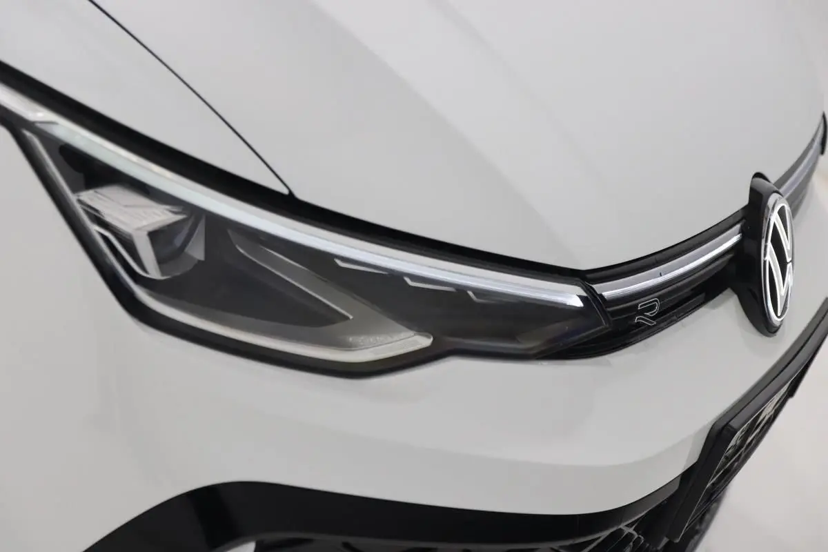 Gros plan sur le phare avant gauche blanc d'une Volkswagen Golf 2.0 TDI R-Line avec logo et calandre noire.