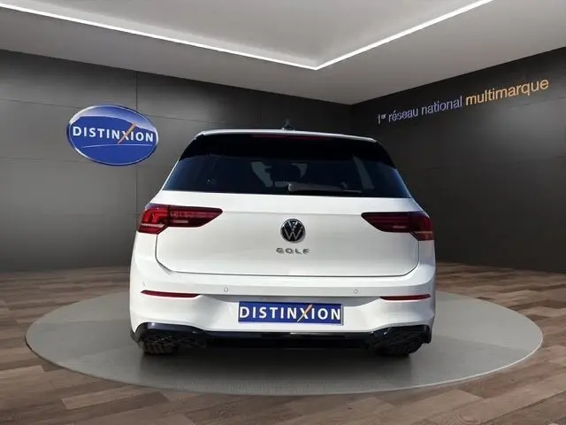 Vue arrière d'une Volkswagen Golf blanche 2025 R-Line avec toit panoramique et caméra 360, en intérieur showroom.