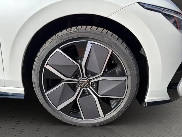 Gros plan sur la roue avant droite d’une Volkswagen Golf blanche avec jante noire et argentée au design moderne.