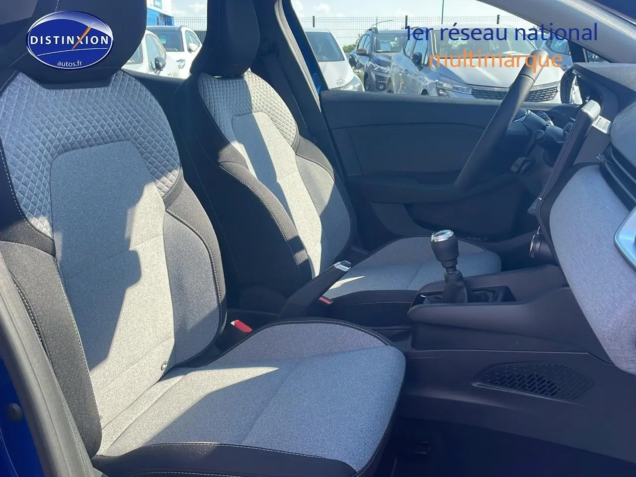 Intérieur avant de la Renault Clio V bleu iron, sièges tissu bicolore gris et noir, volant multifonction et boîte manuelle visible.