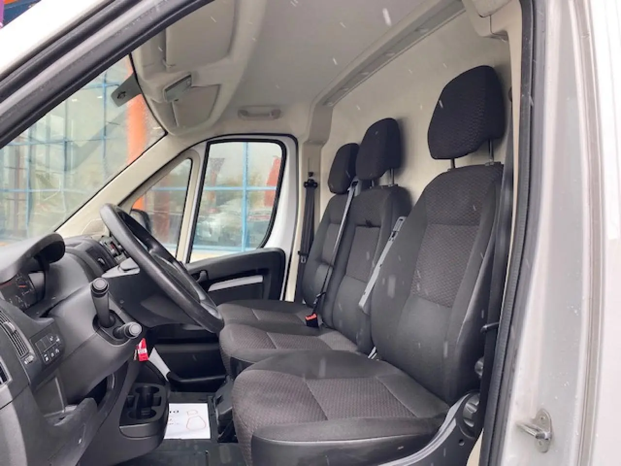 Vue intérieure côté conducteur de l'Opel Movano Fourgon blanc 2023 avec sièges tissu noir et tableau de bord simple.