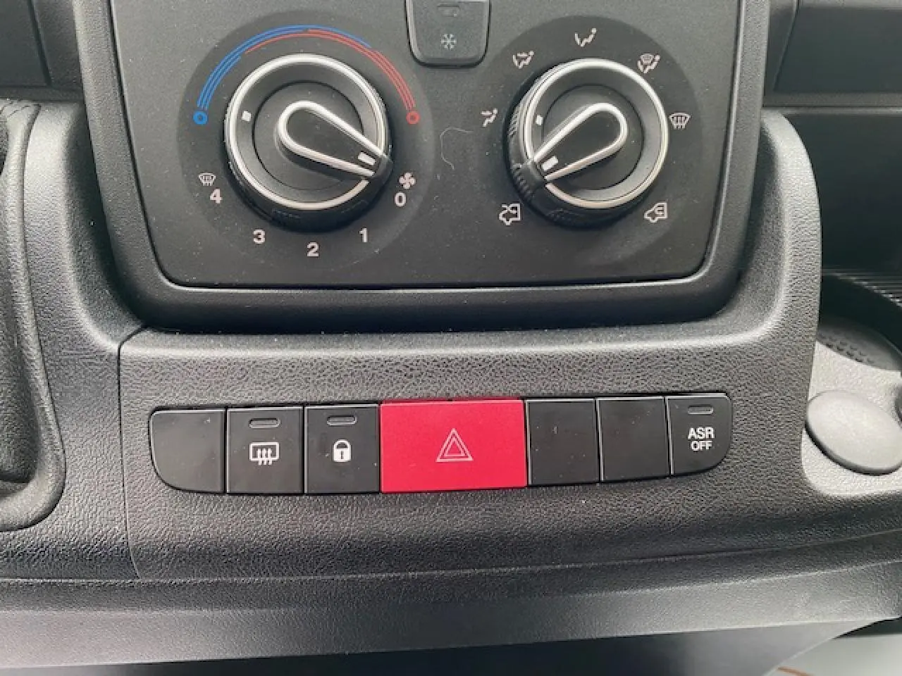 Gros plan sur les commandes de climatisation et les boutons de sécurité du tableau de bord du fourgon Opel Movano blanc.