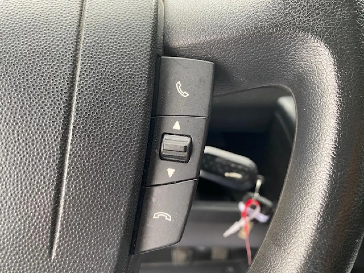 Gros plan sur les commandes Bluetooth du volant noir de l'Opel Movano Fourgon blanc 2023.