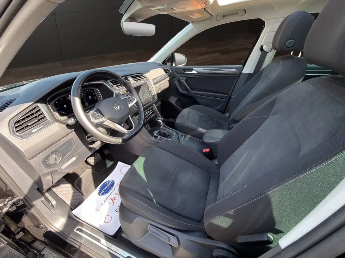 Vue intérieure côté conducteur du Volkswagen Tiguan 2.0 TDI noir, avec volant cuir et écran tactile central.