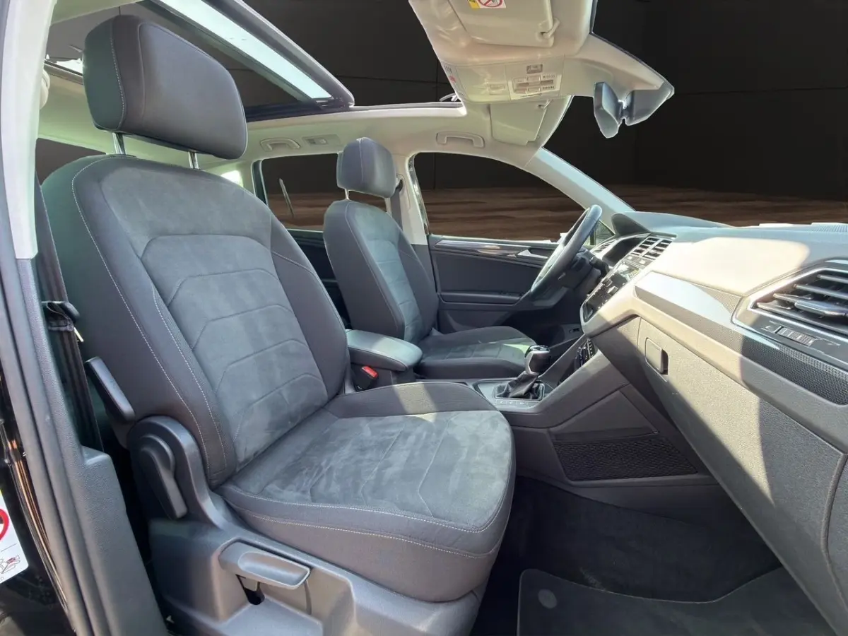 Vue intérieure côté droit du Volkswagen Tiguan noir 2022, sièges avant en tissu gris et toit ouvrant panoramique.